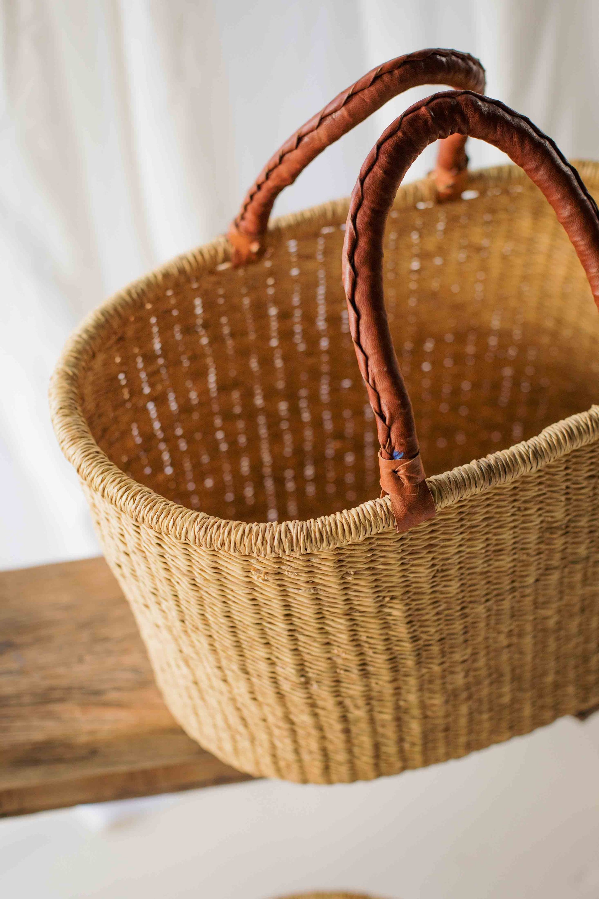 Woven basket with leather handles on a wooden surface
