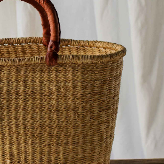 Woven basket with wooden handle on a wooden table against a white curtain background