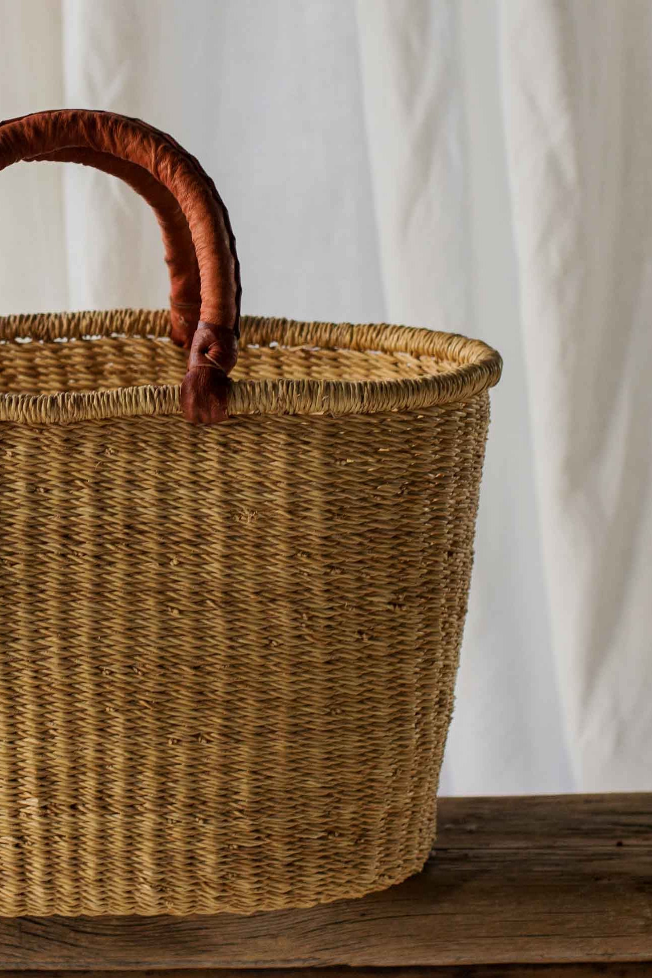 Woven basket with wooden handle on a wooden table against a white curtain background