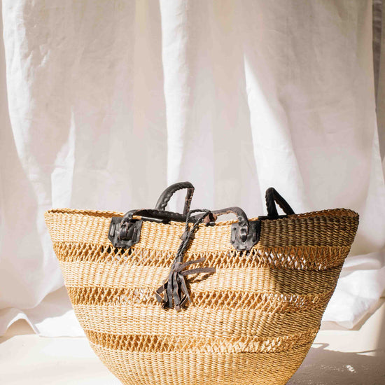 Woven basket with black straps on a white background