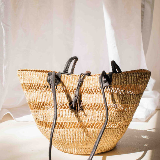 Woven straw bag with black straps on a light background