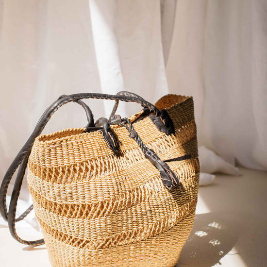 Woven straw bag with leather straps on a light background