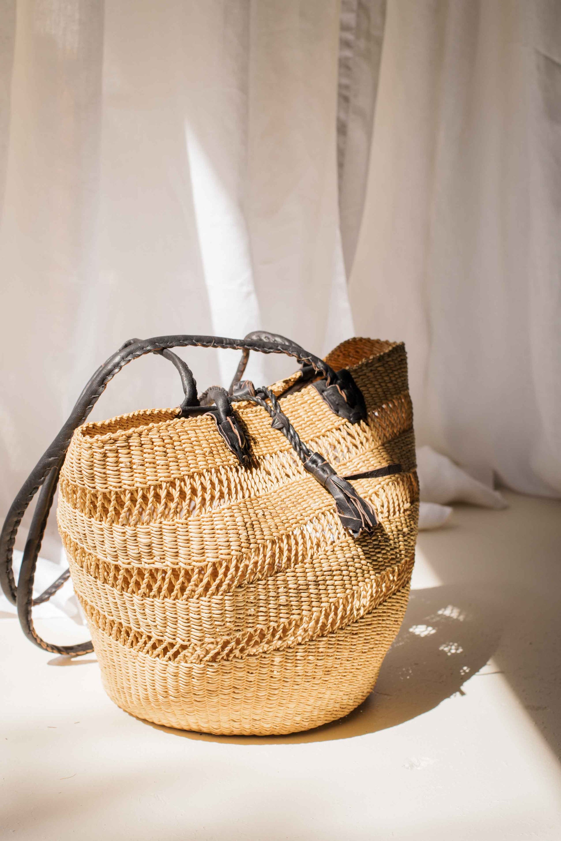 Woven straw bag with leather straps on a light background