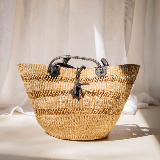 Woven basket with black handles on a light surface with white curtains in the background