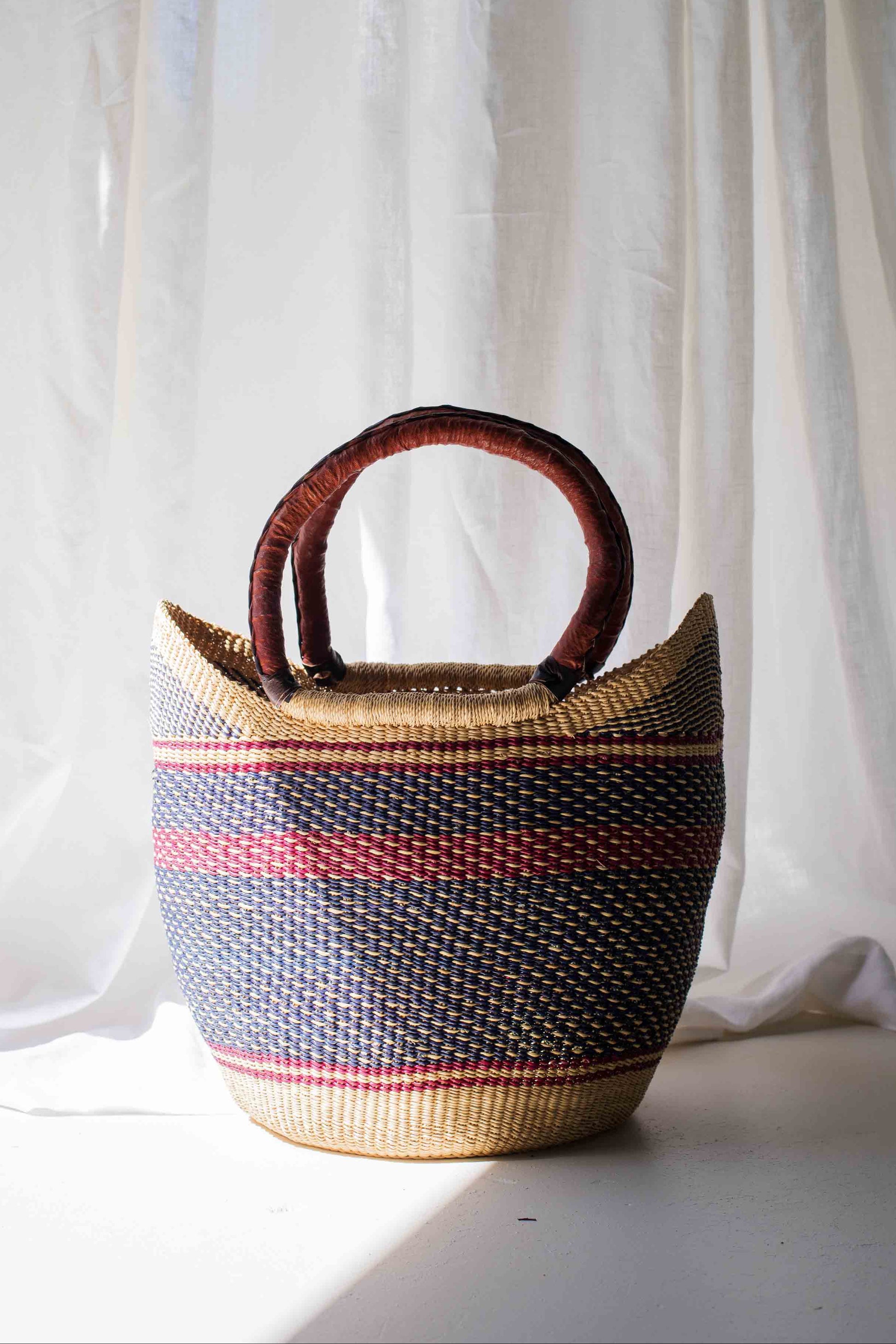 Woven basket with striped pattern against a white curtain background