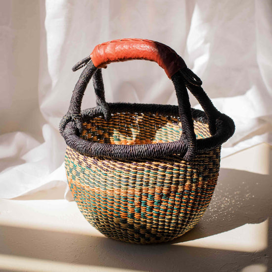 Woven basket with a red handle on a white fabric background
