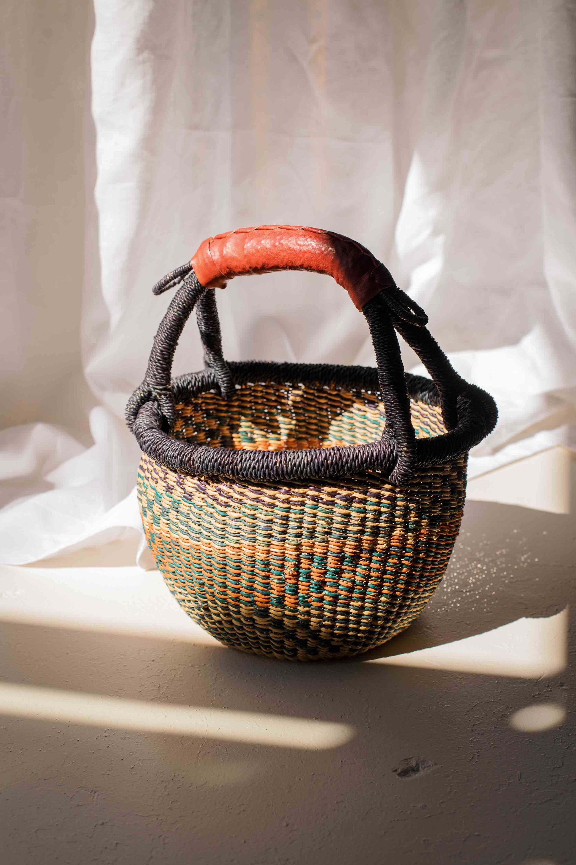 Woven basket with a red handle on a white fabric background