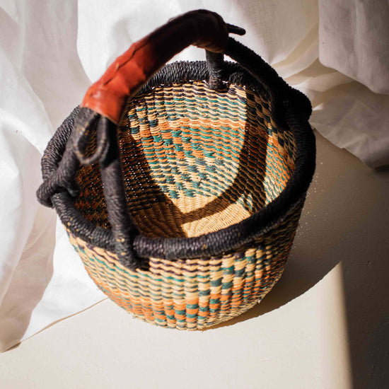 Woven basket with a black handle on a white surface