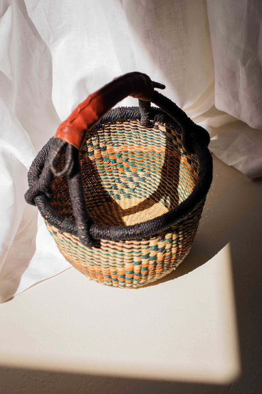 Woven basket with a black handle on a white surface