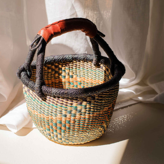 Woven basket with a handle on a light surface with white fabric in the background