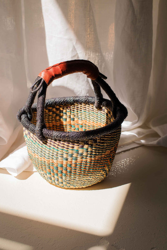 Woven basket with a handle on a light surface with white fabric in the background