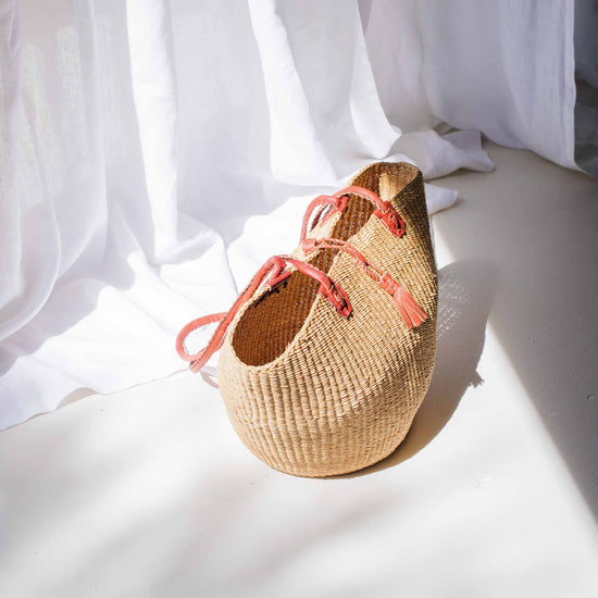 Woven basket with pink straps on a white surface with white curtains in the background