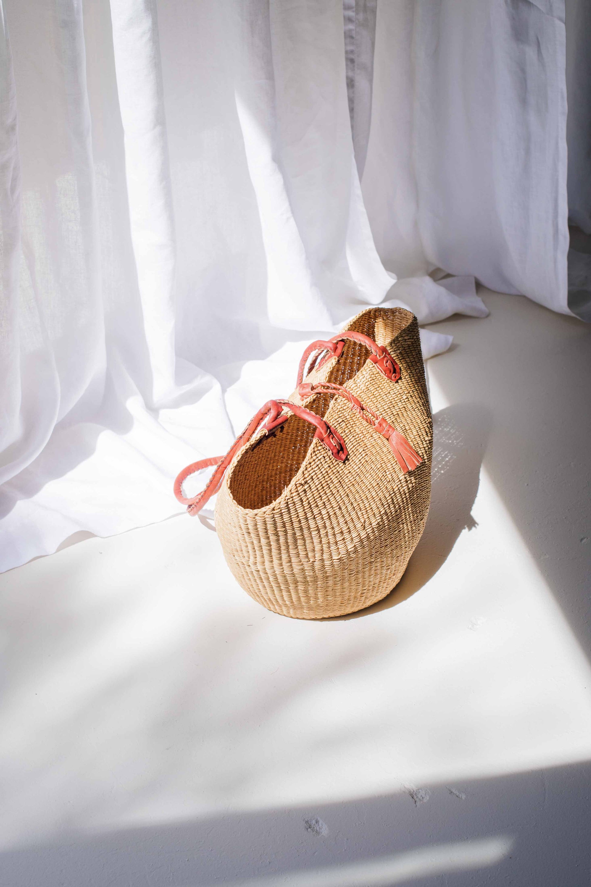 Woven basket with pink straps on a white surface with white curtains in the background