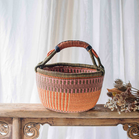 Woven basket with a handle on a wooden table against a white curtain background