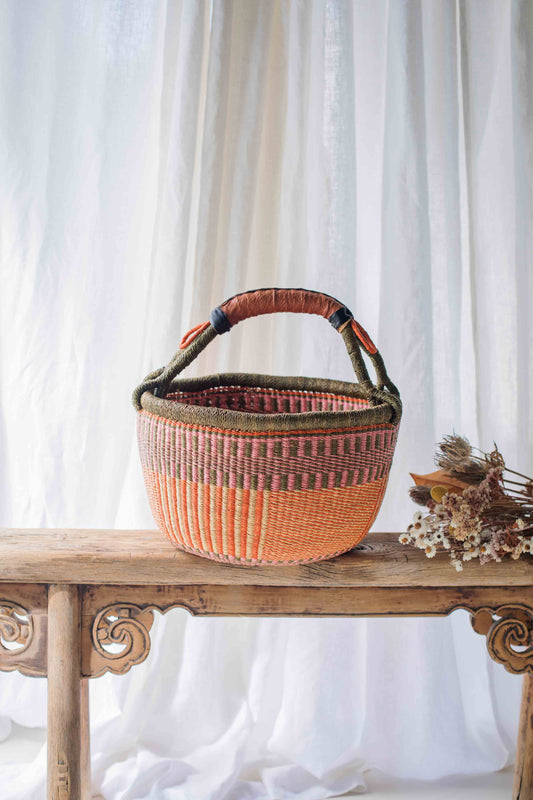 Woven basket with a handle on a wooden table against a white curtain background