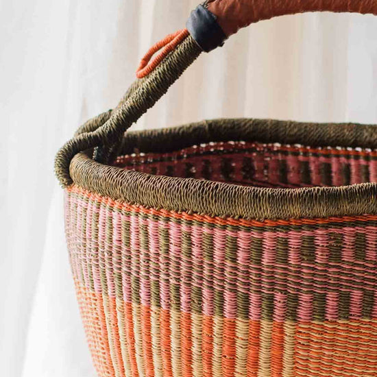 Woven basket with a brown handle on a wooden table against a white curtain background