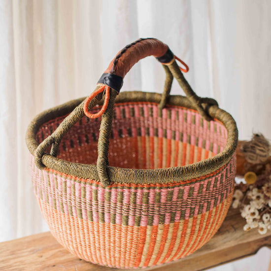Woven basket with pink and brown design on a wooden surface with a white curtain background