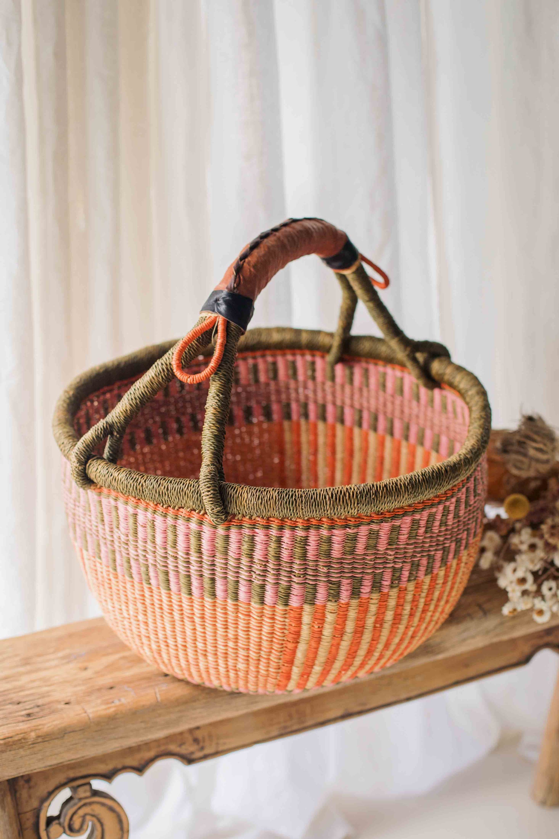 Woven basket with pink and brown design on a wooden surface with a white curtain background
