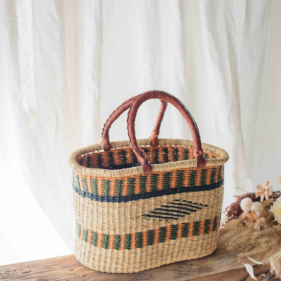 Woven basket with decorative patterns on a wooden bench against a white curtain background