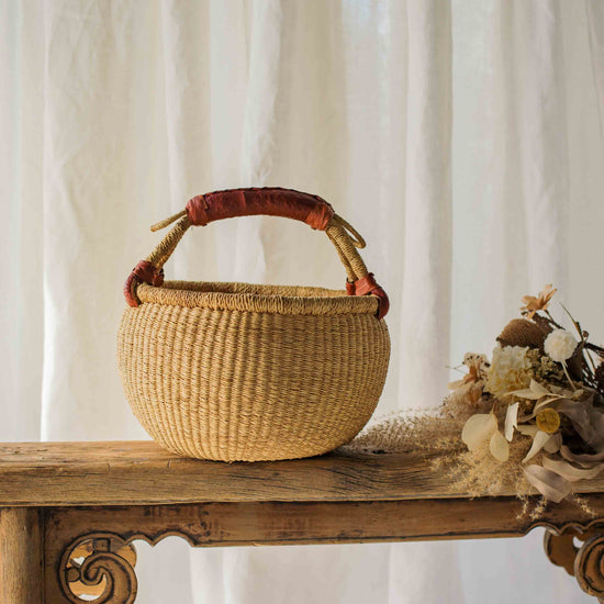 Woven basket with a handle on a wooden table against a white curtain background