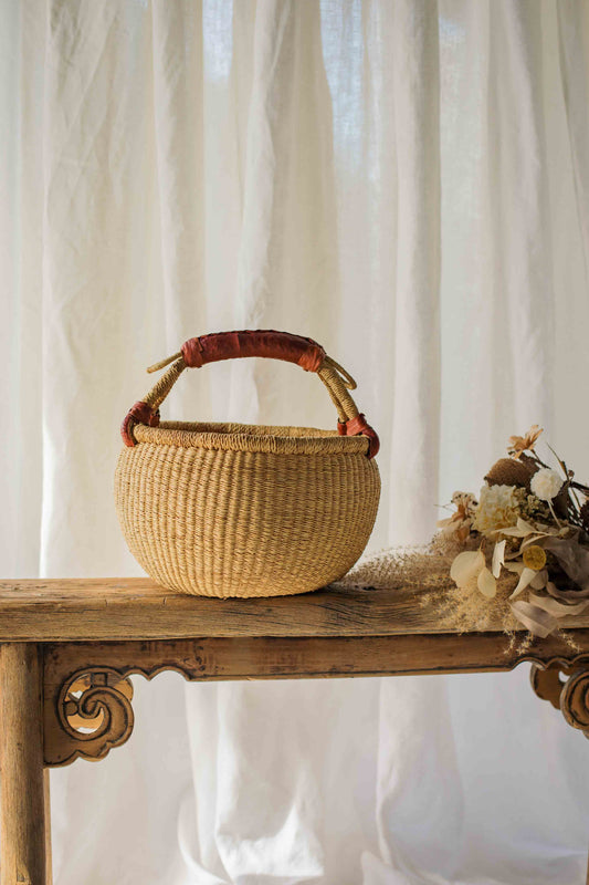 Woven basket with a handle on a wooden table against a white curtain background