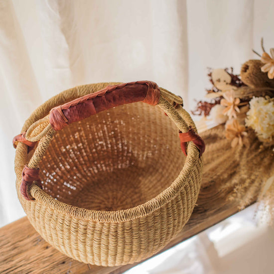 Woven basket with a red handle on a wooden surface with a white background