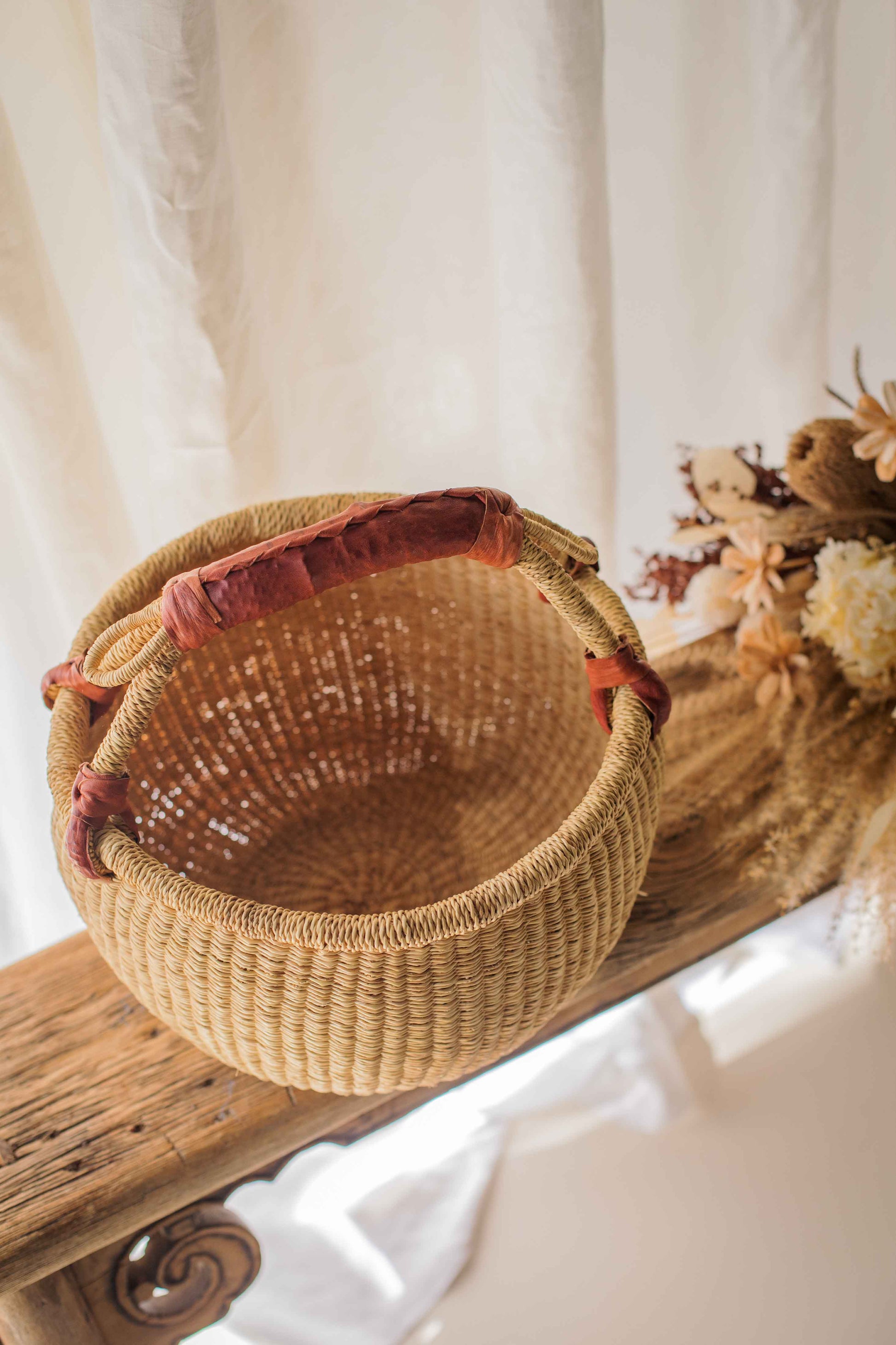 Woven basket with a red handle on a wooden surface with a white background