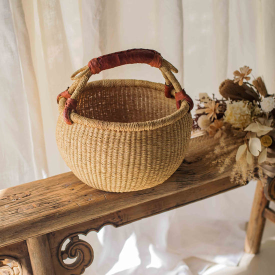 Woven basket with a red handle on a wooden bench against a white curtain background