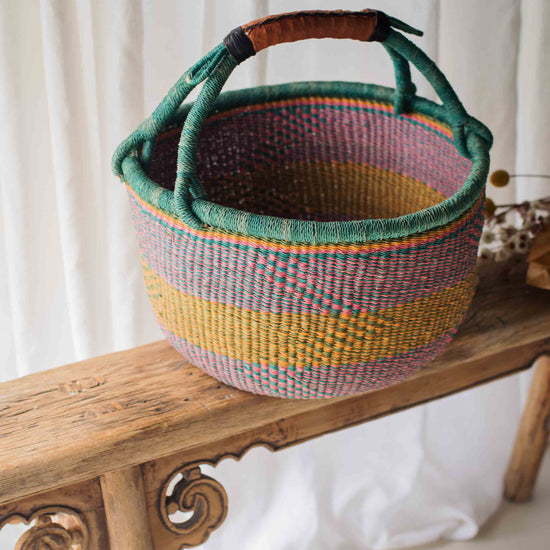 Colorful woven basket with a handle on a wooden bench against a white curtain background