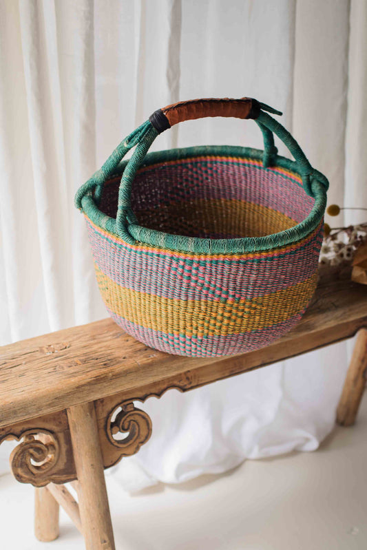 Colorful woven basket with a handle on a wooden bench against a white curtain background