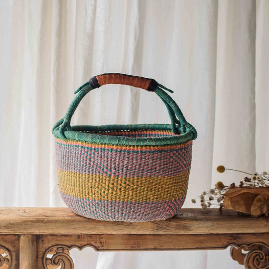 Woven basket with colorful stripes on a wooden table against a white curtain background