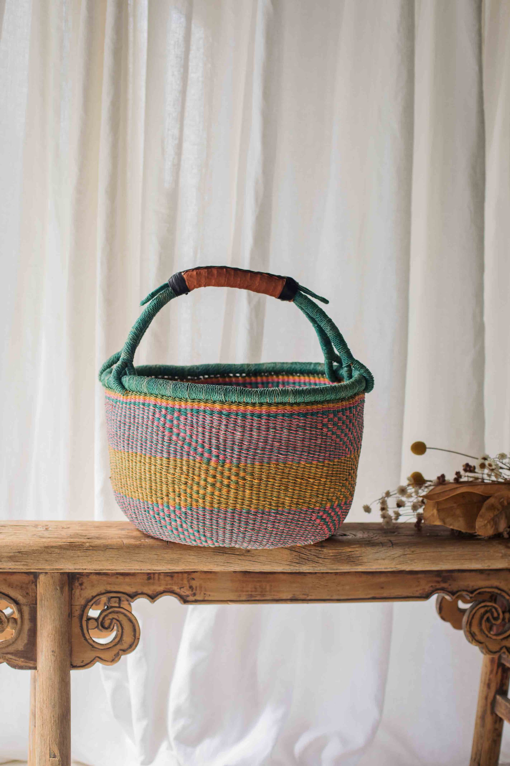 Woven basket with colorful stripes on a wooden table against a white curtain background