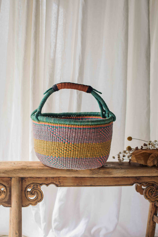 Woven basket with colorful stripes on a wooden table against a white curtain background