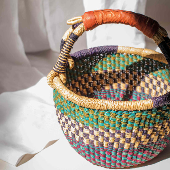 Multicolored woven basket with a patterned handle held by a person wearing a white outfit.