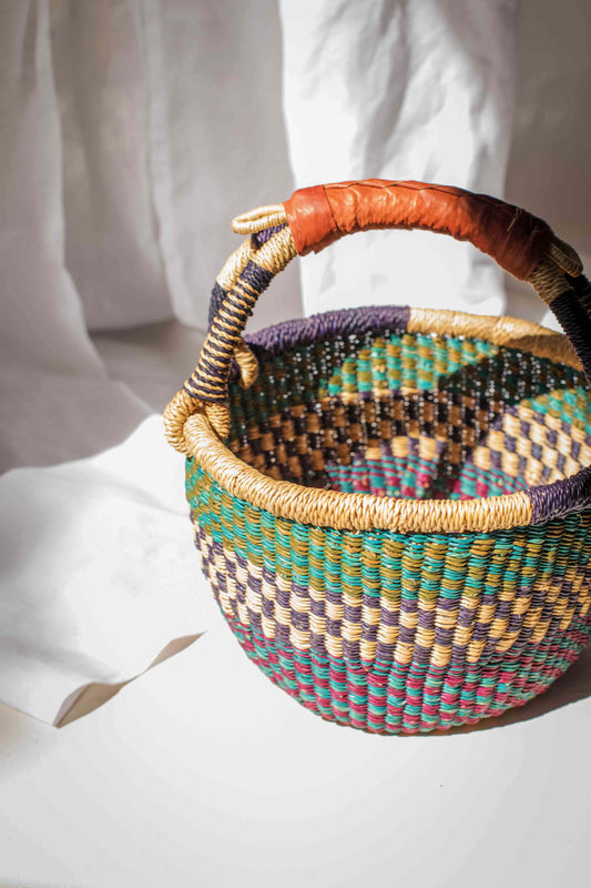 Multicolored woven basket with a patterned handle held by a person wearing a white outfit.