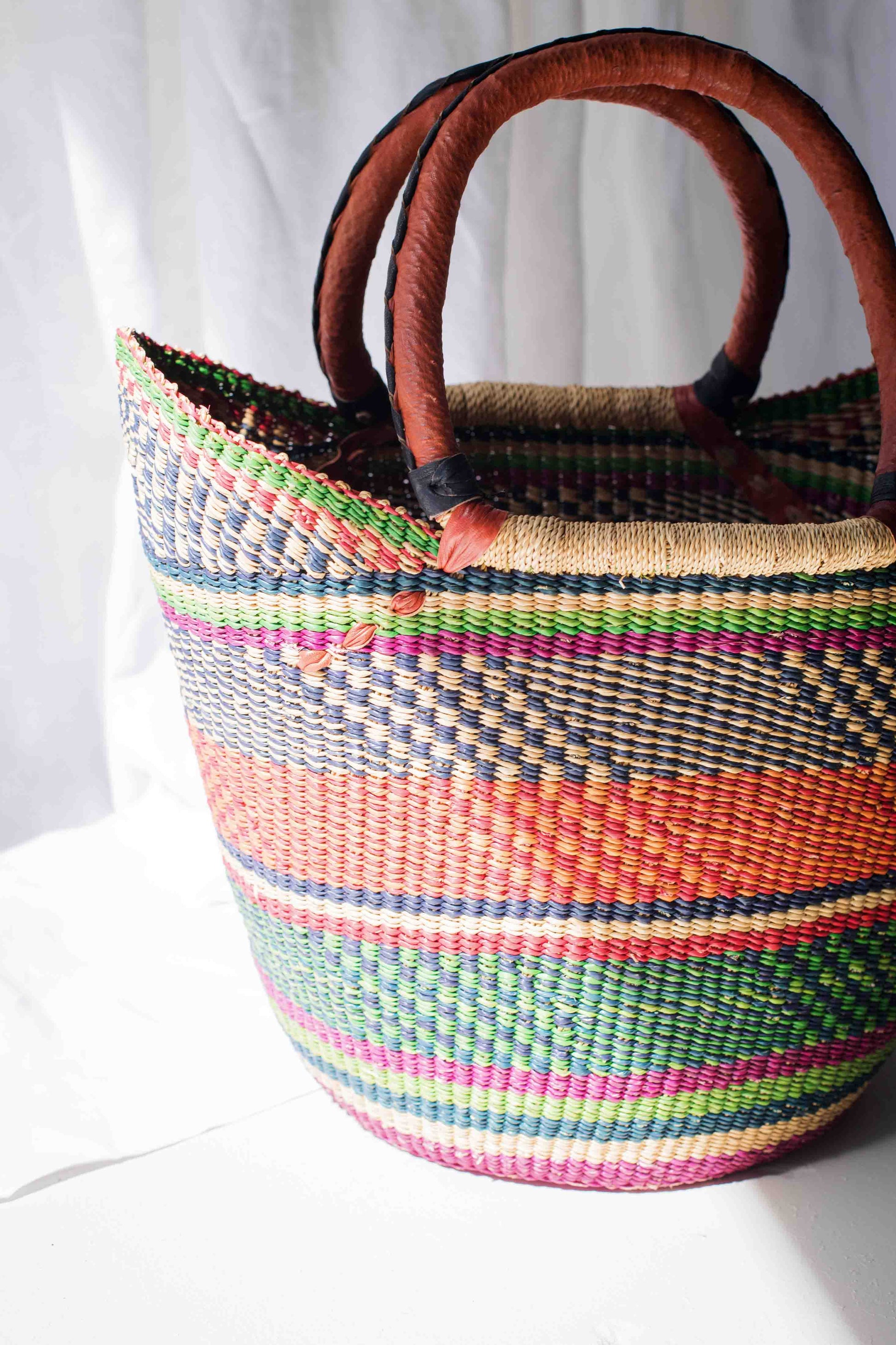Woven basket with colorful stripes and wooden handles on a white background