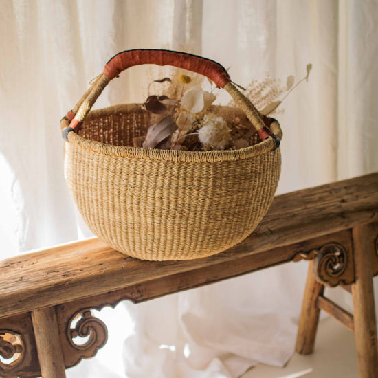 Woven basket with dried flowers on a wooden bench against a white curtain background