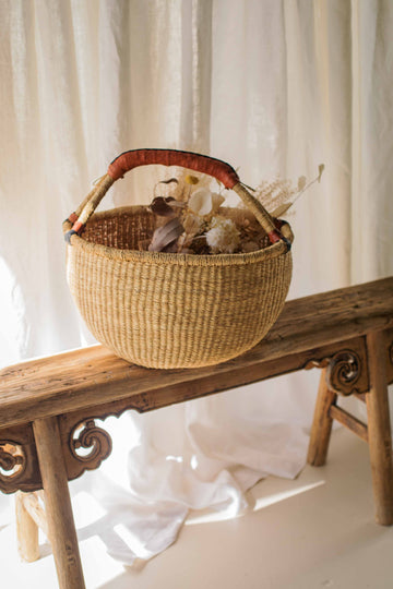 Woven basket with dried flowers on a wooden bench against a white curtain background