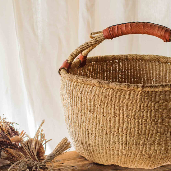 Woven basket with a handle on a wooden table against a white curtain background