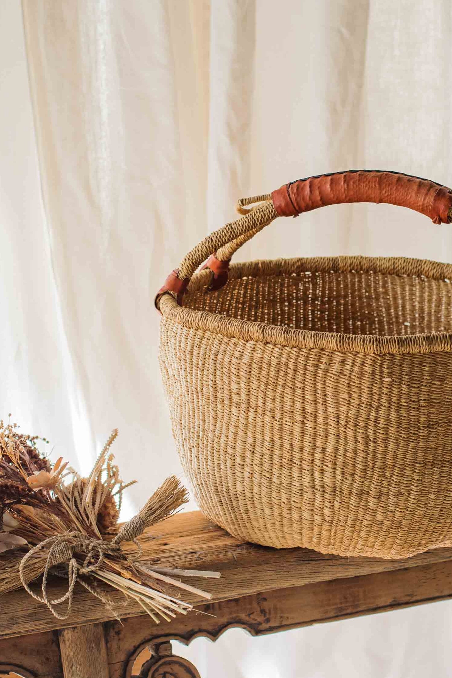 Woven basket with a handle on a wooden table against a white curtain background