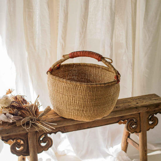 Woven basket on a wooden bench with white curtains in the background