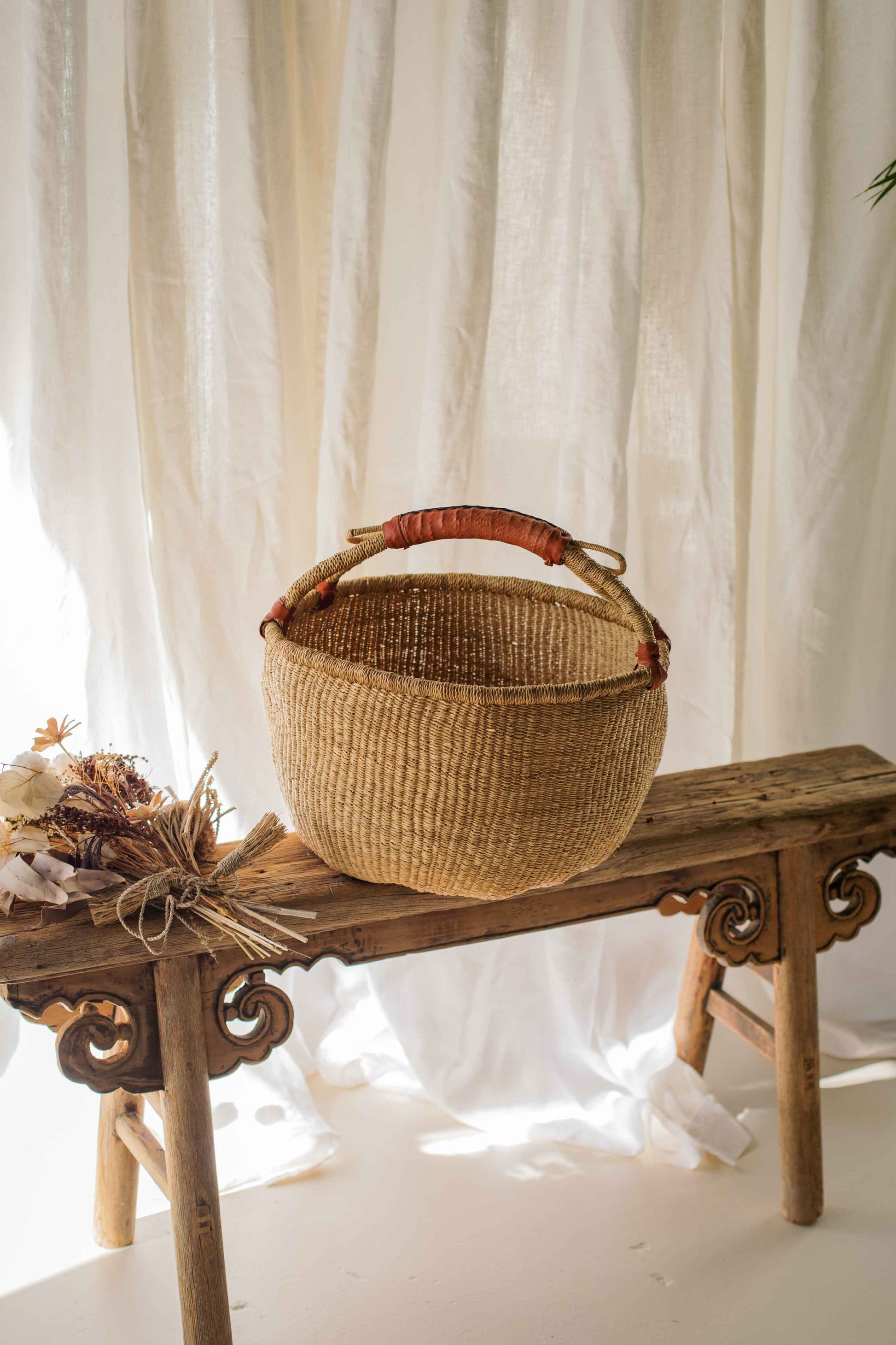 Woven basket on a wooden bench with white curtains in the background
