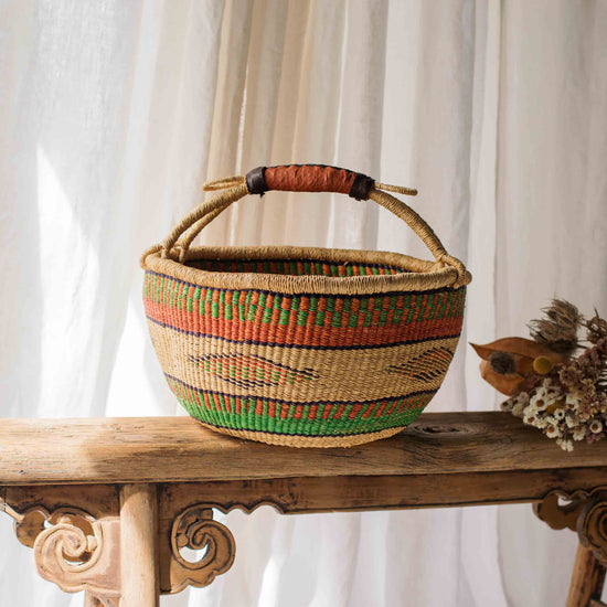 Woven basket with colorful patterns on a wooden table against a white curtain background