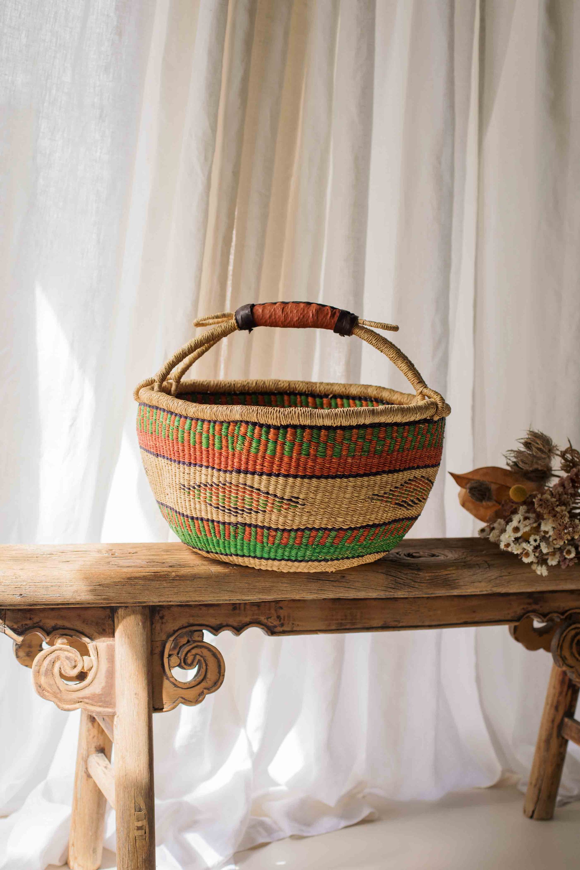 Woven basket with colorful patterns on a wooden table against a white curtain background