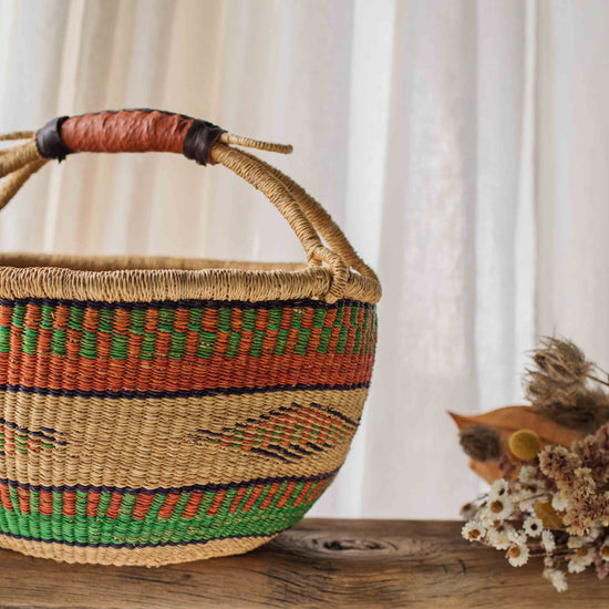 Woven basket with a patterned handle on a wooden surface with a white curtain background