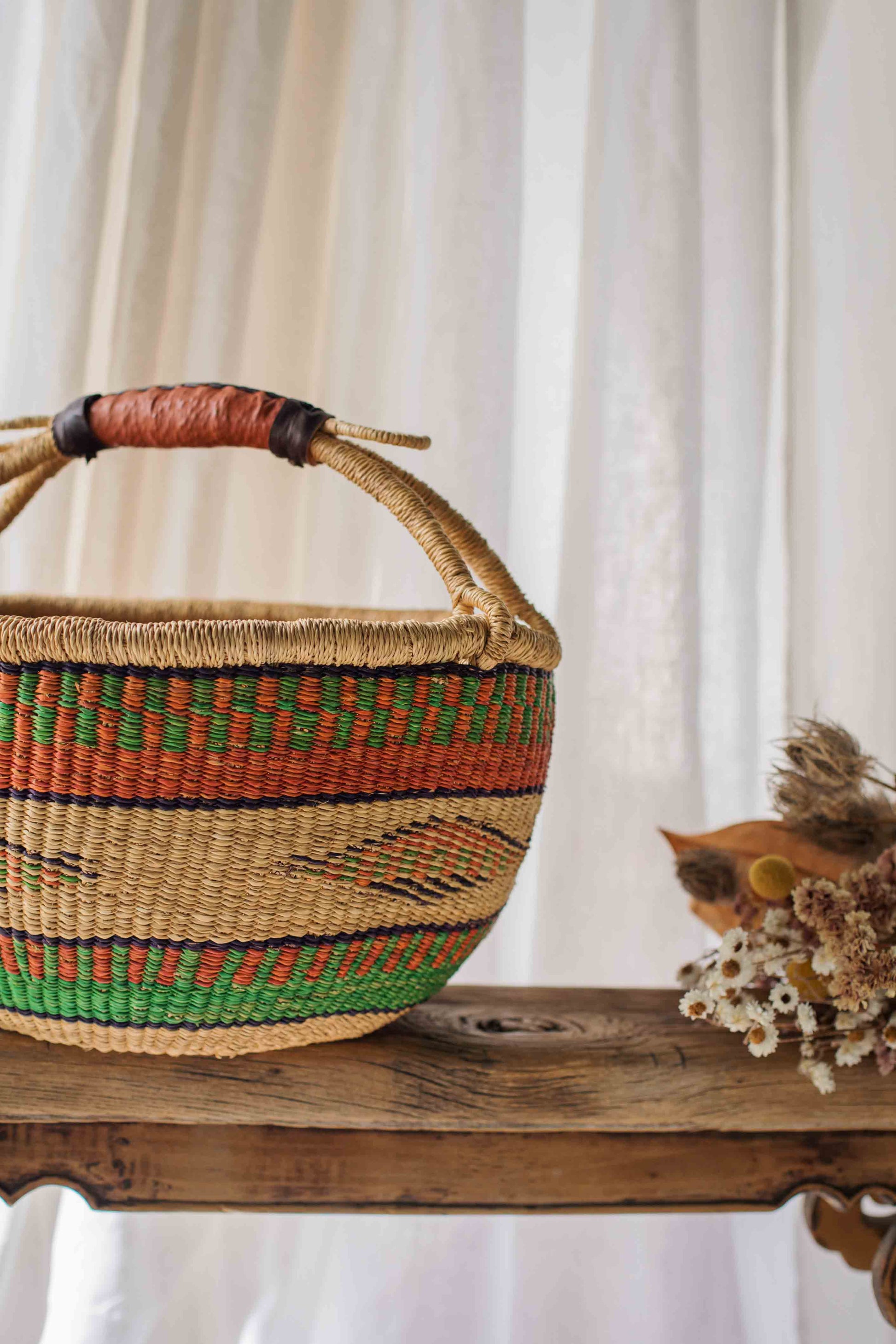Woven basket with a patterned handle on a wooden surface with a white curtain background