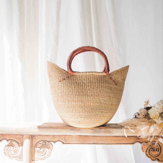 Woven basket with wooden handles on a wooden table with a white curtain background