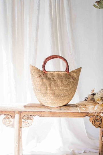 Woven basket with wooden handles on a wooden table with a white curtain background
