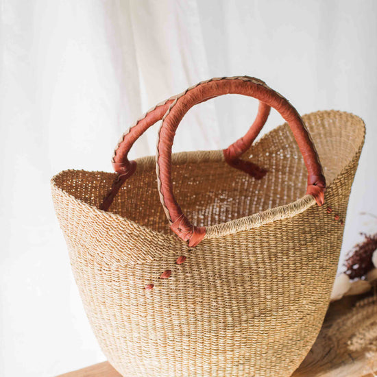 Woven basket with red handles on a wooden surface against a white curtain background