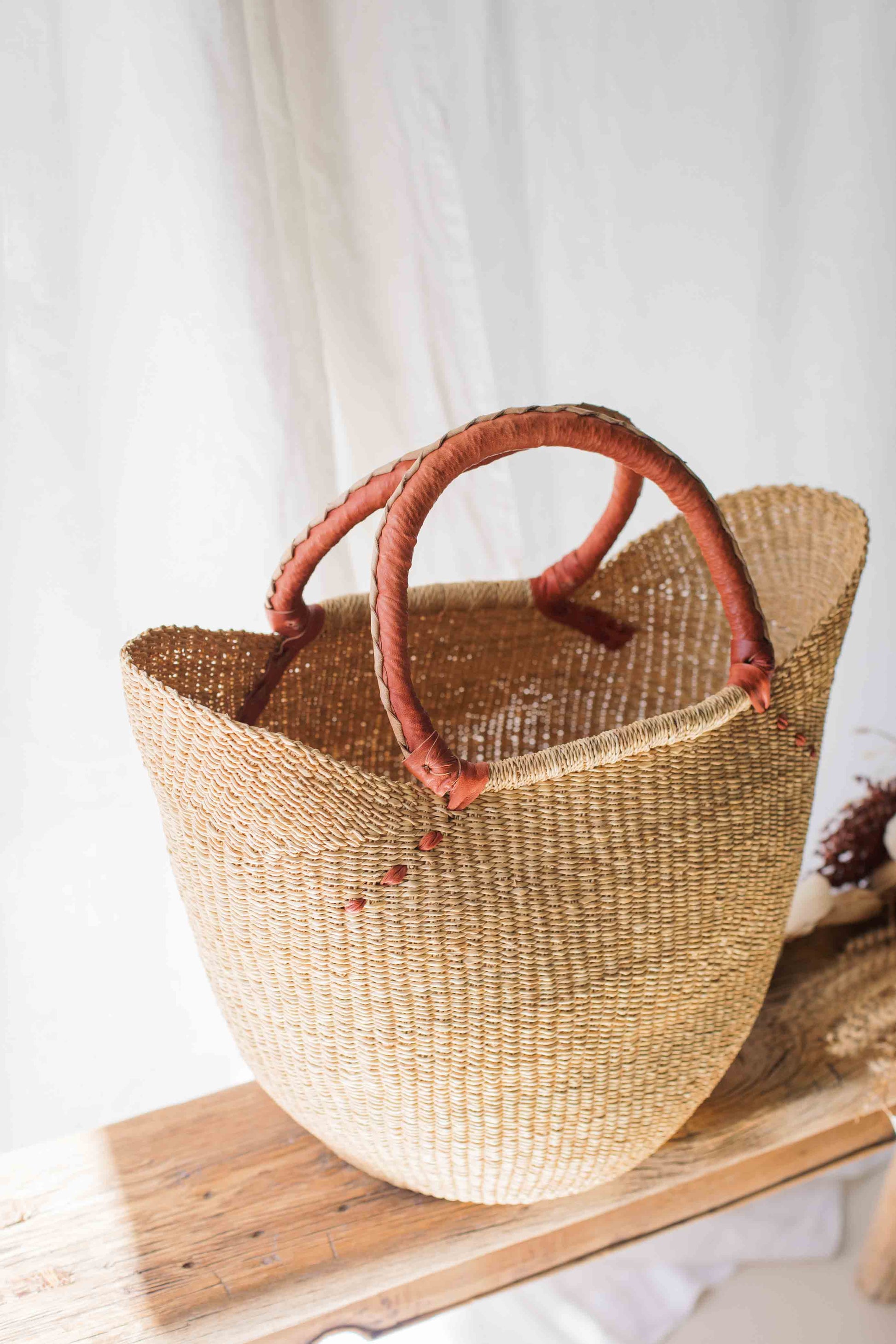 Woven basket with red handles on a wooden surface against a white curtain background